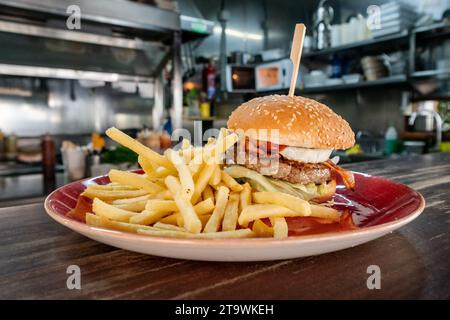 un burger de bœuf complet fraîchement grillé avec bacon et œuf servi avec des frites dans un restaurant fast food. Banque D'Images