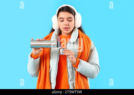 Jeune femme dans les vêtements d'hiver avec thermos sur fond bleu Banque D'Images