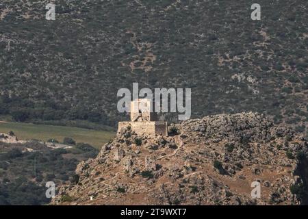 Une ancienne tour de guet mauresque se trouve sur une colline lointaine entourée de milliers d'oliviers dans la vallée autour du village aux murs blancs d'Olvera, Andalousie, Espagne. Banque D'Images