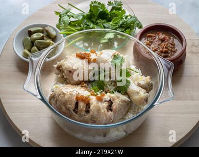 Délicieux poulet à la vapeur au riz (riz au poulet du Hainanais) servir avec de l'ail mariné, du concombre et de la sauce sucrée au Chili sur un plateau rond en bois Aliments halal, Banque D'Images