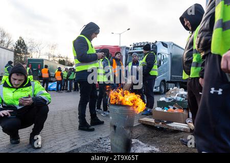 Les chauffeurs de camion ukrainiens se tiennent près d'un feu de joie sur une place de stationnement alors qu'ils attendent dans une file d'attente pour traverser la frontière à Korczowa alors que le syndicat polonais des transports grève et bloque le transport des camions à Korczowa - passage frontalier entre la Pologne et l'Ukraine le 27 novembre 2023. L'Union exige la renégociation des accords de transport entre l'Ukraine et l'Union européenne. Medyka est le quatrième site de grève. Les manifestants n'autorisent que 4 camions commerciaux par heure, ce qui exclut l'aide humanitaire et militaire, le carburant et la nourriture. La grève a commencé le 6 novembre. Les chauffeurs de camion ukrainiens disent qu'ils attendent dans la file d'attente plus de 10 da Banque D'Images