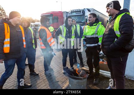 Les chauffeurs de camion ukrainiens se tiennent près d'un feu de joie sur une place de stationnement alors qu'ils attendent dans une file d'attente pour traverser la frontière à Korczowa alors que le syndicat polonais des transports grève et bloque le transport des camions à Korczowa - passage frontalier entre la Pologne et l'Ukraine le 27 novembre 2023. L'Union exige la renégociation des accords de transport entre l'Ukraine et l'Union européenne. Medyka est le quatrième site de grève. Les manifestants n'autorisent que 4 camions commerciaux par heure, ce qui exclut l'aide humanitaire et militaire, le carburant et la nourriture. La grève a commencé le 6 novembre. Les chauffeurs de camion ukrainiens disent qu'ils attendent dans la file d'attente plus de 10 da Banque D'Images