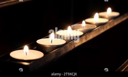 Une rangée de petites bougies votives lumineuses dans une pièce sombre, sanctuaire, église, cathédrale, flammes brûlantes. Lumière dans les ténèbres, espoir. Souvenir et pr Banque D'Images