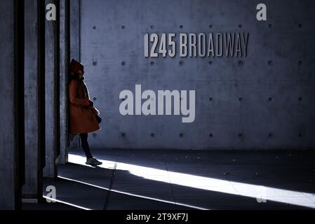 Femme en manteau d'hiver et bonnet penché avec désinvolture contre l'immeuble de bureaux sur Broadway New York City, New York Banque D'Images