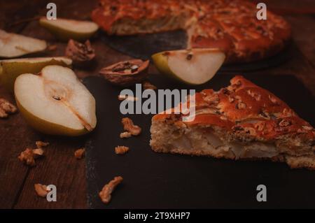 tarte aux poires sur une planche de service noire sur une table en bois, les poires coupées et les noix reposent chaotiquement Banque D'Images