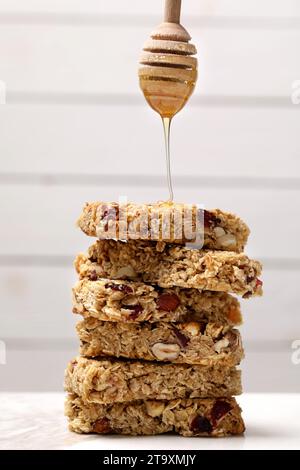 Verser le miel de la Dipper sur la pile de barres de granola savoureuses sur la table blanche Banque D'Images