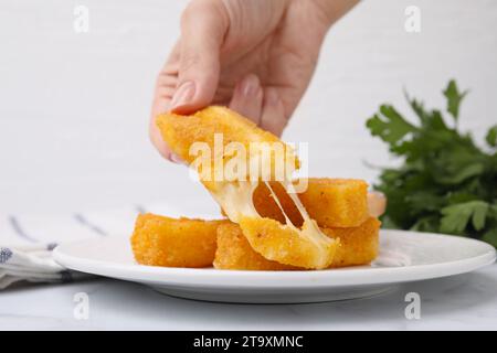 Femme prenant savoureux bâton de mozzarella frit de l'assiette à la table, closeup Banque D'Images