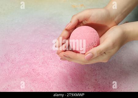 Femme tenant la bombe de bain au-dessus de l'eau avec de la mousse, gros plan. Espace pour le texte Banque D'Images