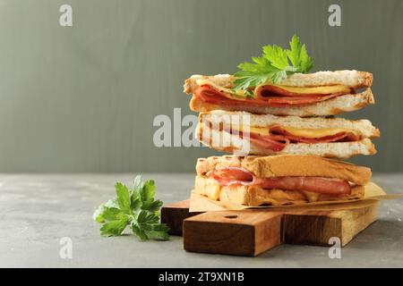 Pile de sandwichs savoureux avec jambon, persil et fromage fondu sur la table grise. Espace pour le texte Banque D'Images