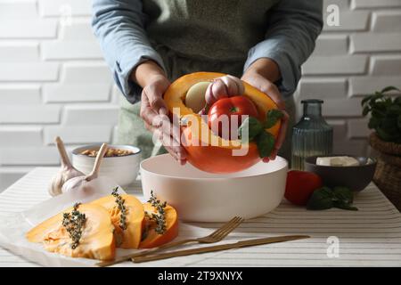 Femme mettant la citrouille farcie avec différents légumes dans le plat de cuisson à table, closeup Banque D'Images