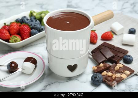 Pot à fondue avec chocolat, guimauves, différentes baies et fourchettes sur table en marbre blanc Banque D'Images