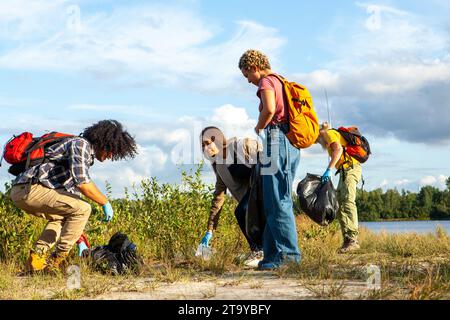 La photographie montre un groupe assidu de bénévoles engagés dans une activité de nettoyage, démontrant ainsi leur engagement envers la santé environnementale. Chaque individu est équipé de gants et de sacs, enlevant soigneusement la litière du paysage naturel. Leurs actions ciblées sous le ciel ouvert, près de l'eau, reflètent un engagement collectif à préserver la beauté et l'intégrité de l'environnement extérieur pour les générations futures. Dévouement à l'environnement : action de nettoyage de groupe. Photo de haute qualité Banque D'Images