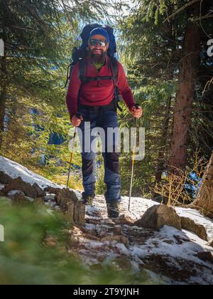Homme barbu avec un sac à dos randonnées dans les montagnes en hiver. Beau temps sur une journée ensoleillée d'hiver en plein air dans les montagnes Banque D'Images