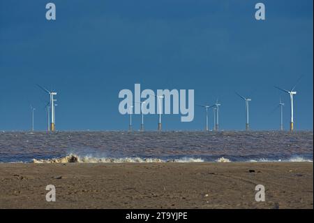 Un parc éolien au large de la côte de Skegness avec des vagues brisantes sur la plage pendant la saison d'hiver Banque D'Images