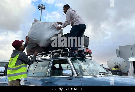 Rafah, Égypte. 27 novembre 2023. Un chauffeur emmenant des Palestiniens à la frontière pour rentrer dans la bande de Gaza se tient debout sur sa voiture et décharge ses bagages au poste frontière de Rafah. Peu d'endroits sont aussi symboliquement chargés dans la guerre de Gaza que le poste frontière égyptien de Rafah. (À dpa 'atteindre la frontière : une visite au point de passage de Rafah') crédit : Johannes Sadek/dpa/Alamy Live News Banque D'Images