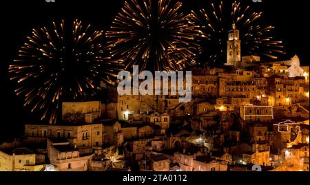 Vue panoramique des pierres typiques (Sassi di Matera) et l'église de Matera la nuit, avec lumière de feu d'artifice de célébration scintillant abstrait doré Banque D'Images