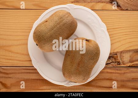 Deux kiwis mûrs sur une assiette en céramique blanche sur une table en bois, macro, vue de dessus. Banque D'Images