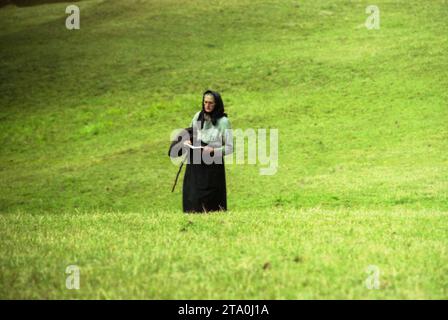 Comté de Gorj, Roumanie, 2000. Femme âgée seule sur un terrain lisant d'un livre de prières. Banque D'Images