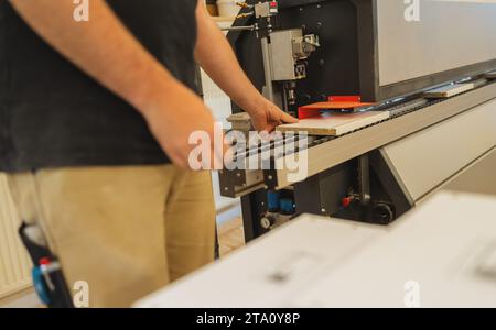 Travailleur plaçant des feuilles de contreplaqué sur la machine de découpe dans un atelier Banque D'Images