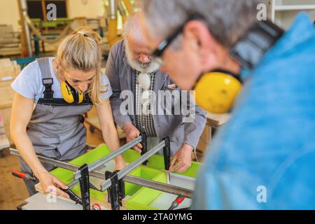 Trois menuisiers avec protection auditive travaillant sur une pièce de bois serrée dans un atelier Banque D'Images