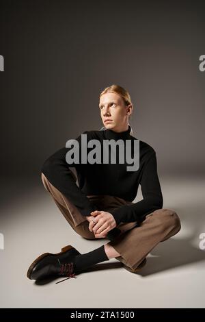 personne attrayante non binaire avec queue de cheval assis sur le sol avec les jambes croisées et regardant loin Banque D'Images