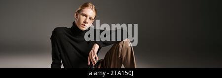 personne attrayante non binaire en col roulé noir assis sur le sol et regardant la caméra, bannière Banque D'Images