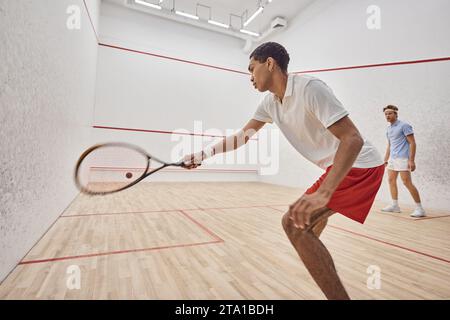 jeunes hommes multiculturels actifs jouant au squash à l'intérieur du court, défi et motivation Banque D'Images