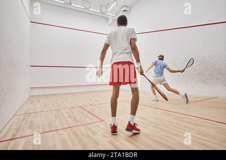 hommes actifs interraciaux en vêtements de sport jouant au squash à l'intérieur du court, défi et motivation Banque D'Images