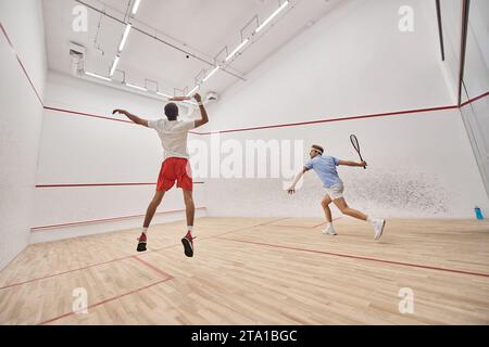 sportifs interraciaux jeunes et actifs en sportswear sautant tout en jouant au squash à l'intérieur du court Banque D'Images