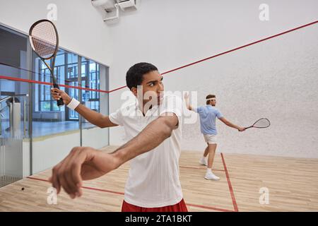 jeunes joueurs interraciaux en tenue active jouant au squash ensemble à l'intérieur du court, style de vie Banque D'Images