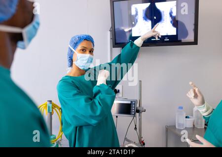 Chirurgiens masculins et féminins avec masques faciaux regardant les rayons X dans la salle d'opération de l'hôpital Banque D'Images