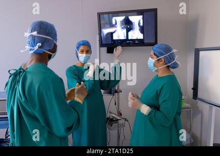 Chirurgiens masculins et féminins avec masques faciaux regardant les rayons X dans la salle d'opération de l'hôpital Banque D'Images