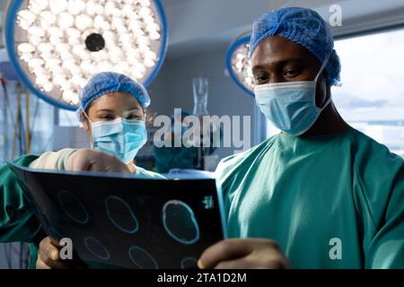 Chirurgiens masculins et féminins avec masques faciaux regardant les rayons X dans la salle d'opération de l'hôpital Banque D'Images