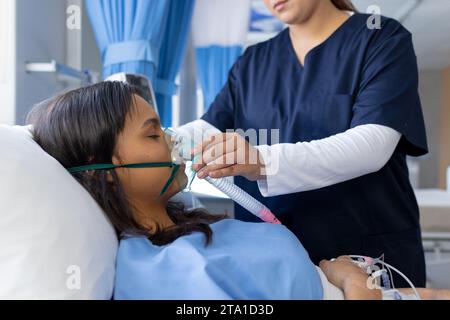 Médecin biracial appliquant un masque à oxygène à la patiente dans son lit en chambre d'hôpital Banque D'Images