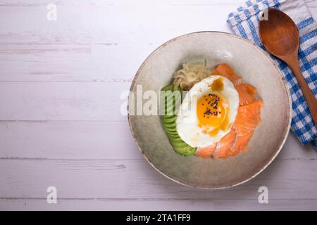 Donburi de saumon teriyaki avec œuf au plat, avocat, oignon, poivron rouge et autres légumes. Plat typiquement japonais. Banque D'Images