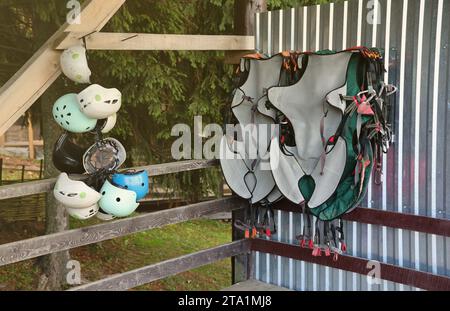 Équipement d'escalade - casques colorés et gilets de sécurité accrochés à une planche dans un parc de corde en gros plan Banque D'Images