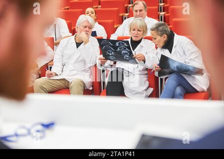 Professionnels masculins et féminins examinant les rayons X pendant qu'ils étaient assis dans le public pendant une conférence médicale à l'auditorium Banque D'Images