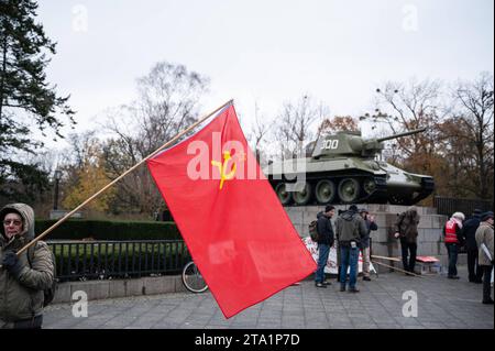 25.11.2023, Berlin, Deutschland, Europa - im Vorfeld einer Friedensdemonstration steht ein Demonstrant mit roter sowjetischer Flagge am Sowjetischen Ehrenmal im Ortsteil Tiergarten mit einem T-34 Panzer im hintergrund. Einige tausend Menschen demonstrieren am Brandenburger Tor im Berliner Bezirk Mitte fuer den Frieden unter dem Titel Nein zu Kriegen- Ruestungswahnsinn stoppen - Zukunft friedlich und gerecht gestalten . Eine der zentralen Forderungen der Kundgebung sind Verhandlungen mit Russland. Auf der Demonstration sprachen neben der Hauptrednerin und ehemaligen Linken-Politikerin Sahra Wag Banque D'Images