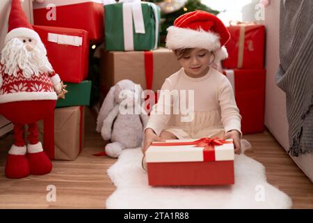 Adorable fille déballage cadeau assis près de l'arbre de noël à la maison Banque D'Images