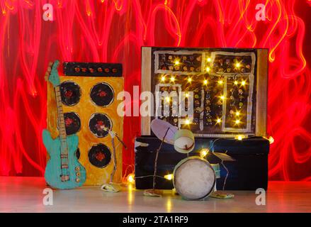 Modèles grungy en carton de synthétiseur, kit de batterie, guitare, amplificateur et microphone sur scène avec des traînées de lumière sauvage, musique, performance, concept d'instruments, Banque D'Images