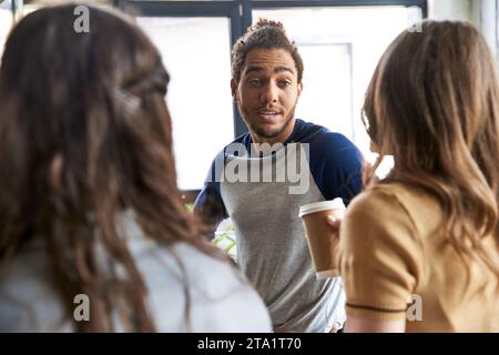 homme afro-américain excité parlant et partageant des idées avec des collègues féminines au bureau, travail d'équipe Banque D'Images