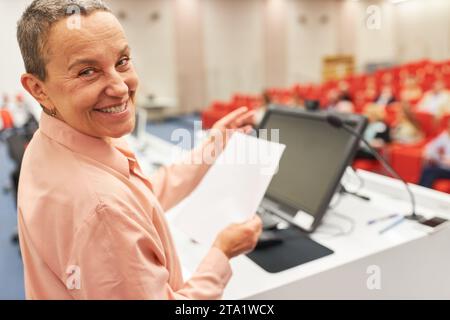 Portrait de la femme conférencière tenant le document à la conférence d'affaires en gestant tout en discutant avec l'auditoire Banque D'Images