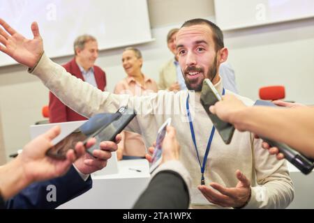 Haut-parleur d'affaires masculin faisant des gestes tout en parlant aux journalistes avec des microphones et des téléphones lors de la conférence de presse Banque D'Images