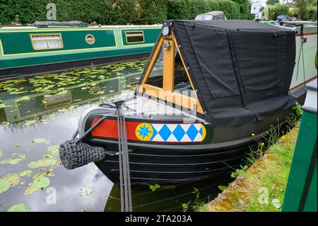 Cordes noires attachées à la proue d'un bateau étroit amarré sur une branche de canal tranquille parmi d'autres bateaux étroits et de l'herbe d'eau flottante. Banque D'Images