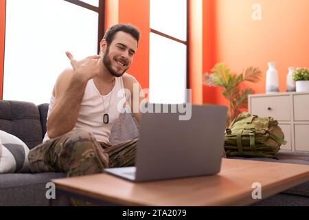 Jeune homme hispanique portant l'uniforme de l'armée de camouflage faisant appel vidéo à la maison souriant heureux pointant avec la main et le doigt Banque D'Images