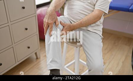 Les mains de l'homme âgé touchent le genou dans la douleur, souffrant dans la clinique de réadaptation pendant le traitement de physiothérapie Banque D'Images