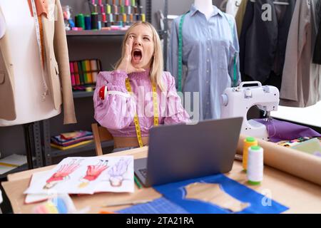 Jeune femme caucasienne couturière designer utilisant un ordinateur portable désemparé et confondu avec les bras ouverts, aucune idée et visage douteux. Banque D'Images