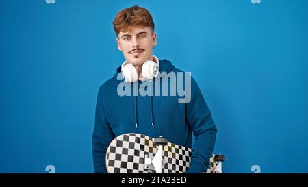 Jeune homme hispanique tenant le patin portant des écouteurs célébrant sur fond bleu isolé Banque D'Images