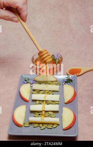 Femme saupoudre une cuillère en bois avec du miel sur un plateau avec du fromage, de la pomme et des noix Banque D'Images