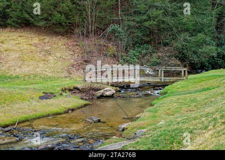 Vieux pont rustique en bois sur une partie peu profonde de ruisseau d'un sentier à travers le parc le long de la colline des arbres en hiver Banque D'Images